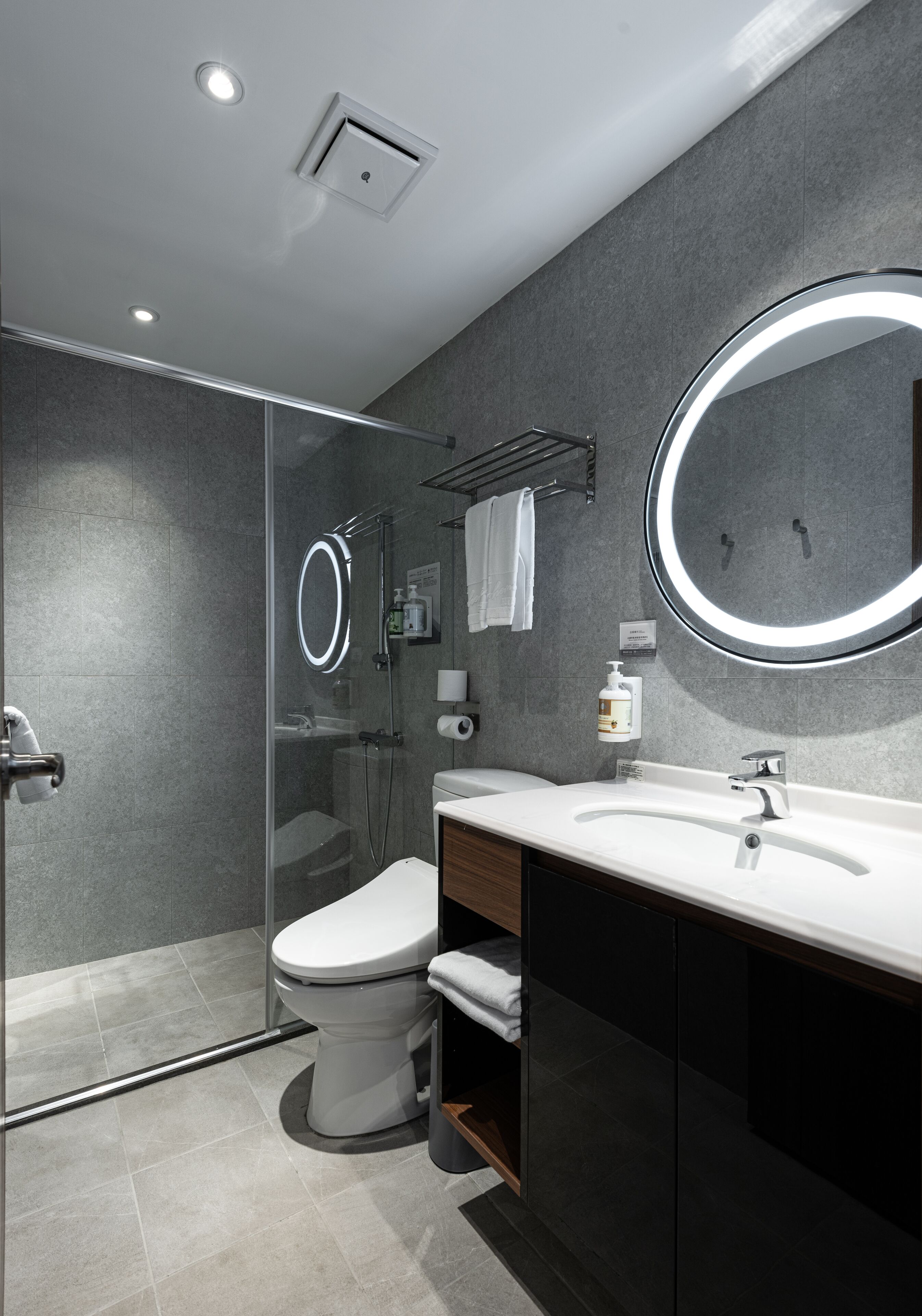 Ein modernes Badezimmer mit einer gläsernen Duschkabine, einer weißen Toilette, einem Waschtisch mit Spiegel und einem Handtuchhalter.