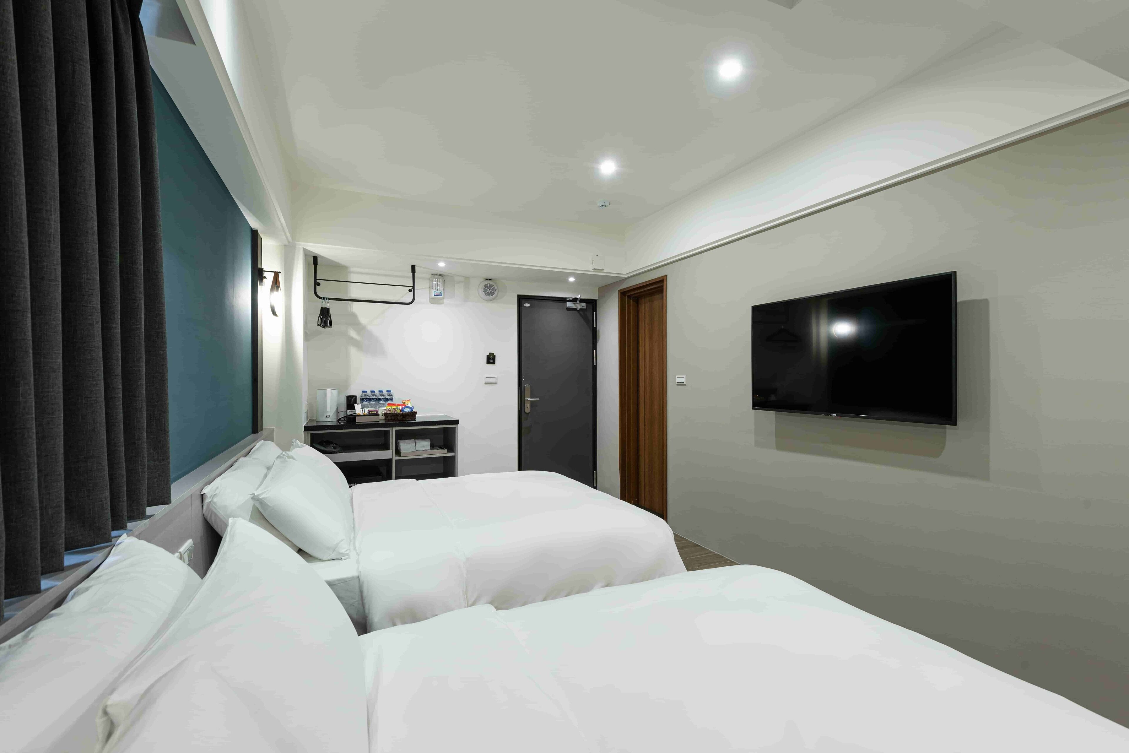 Une chambre d’hôtel avec deux lits, une télévision, un bureau avec une chaise et une porte.