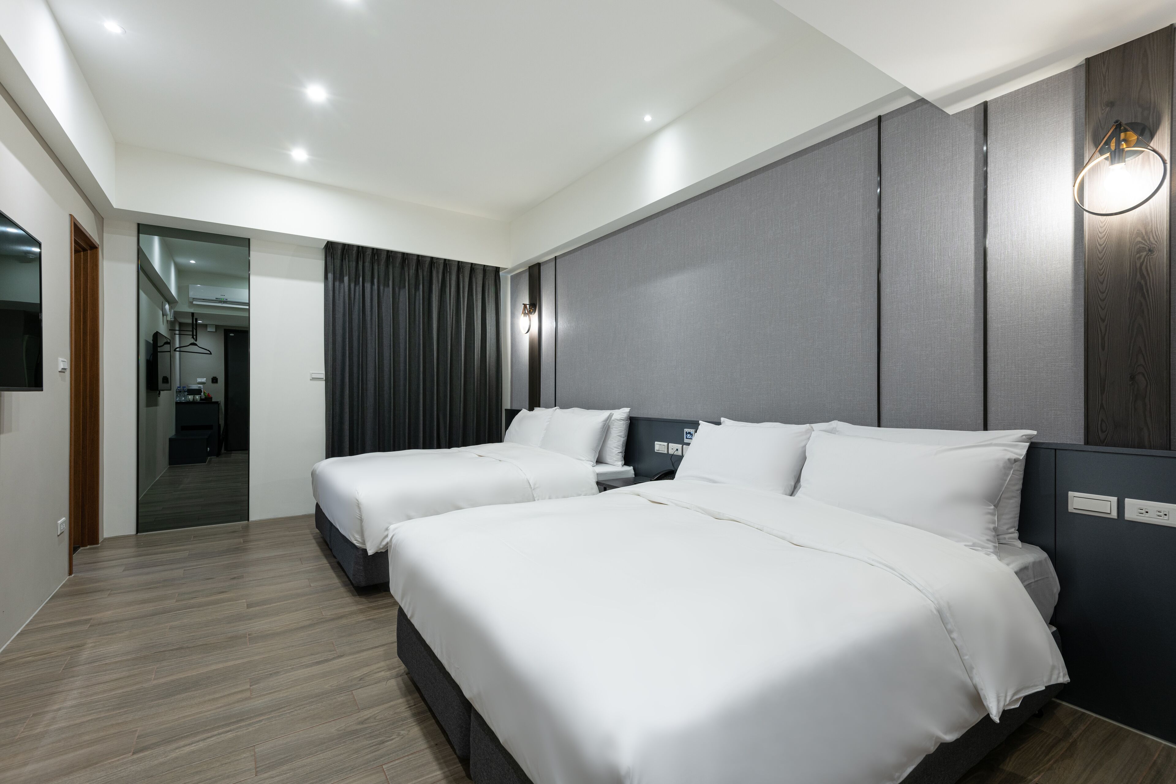 A modern hotel room with two beds, a flat-screen TV, and a walk-in closet.