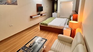 A modern hotel room with a bed, a sofa, a TV, and a small table.
