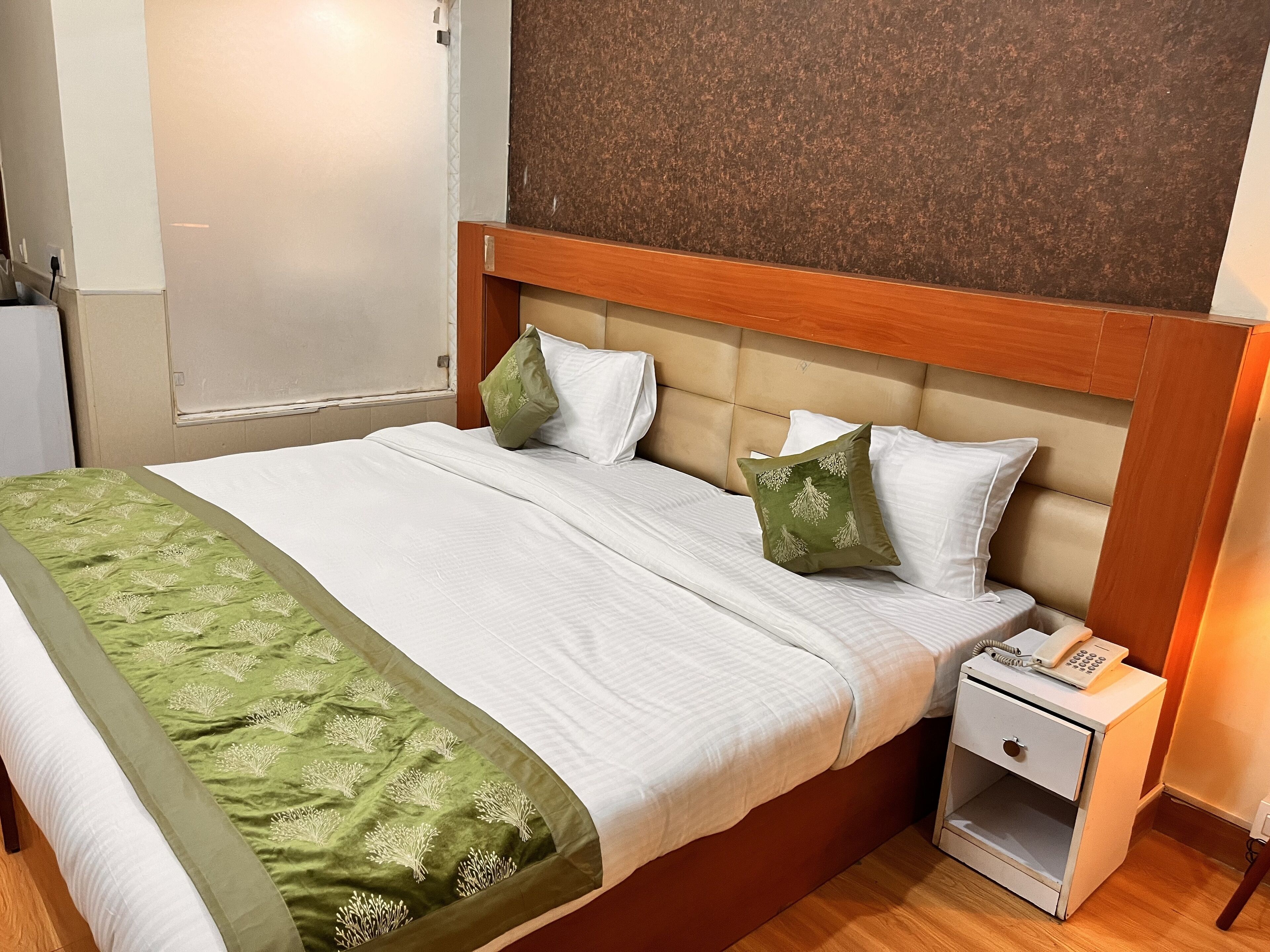 A neatly made bed with a green and white bedspread, two white pillows, and a wooden headboard.
