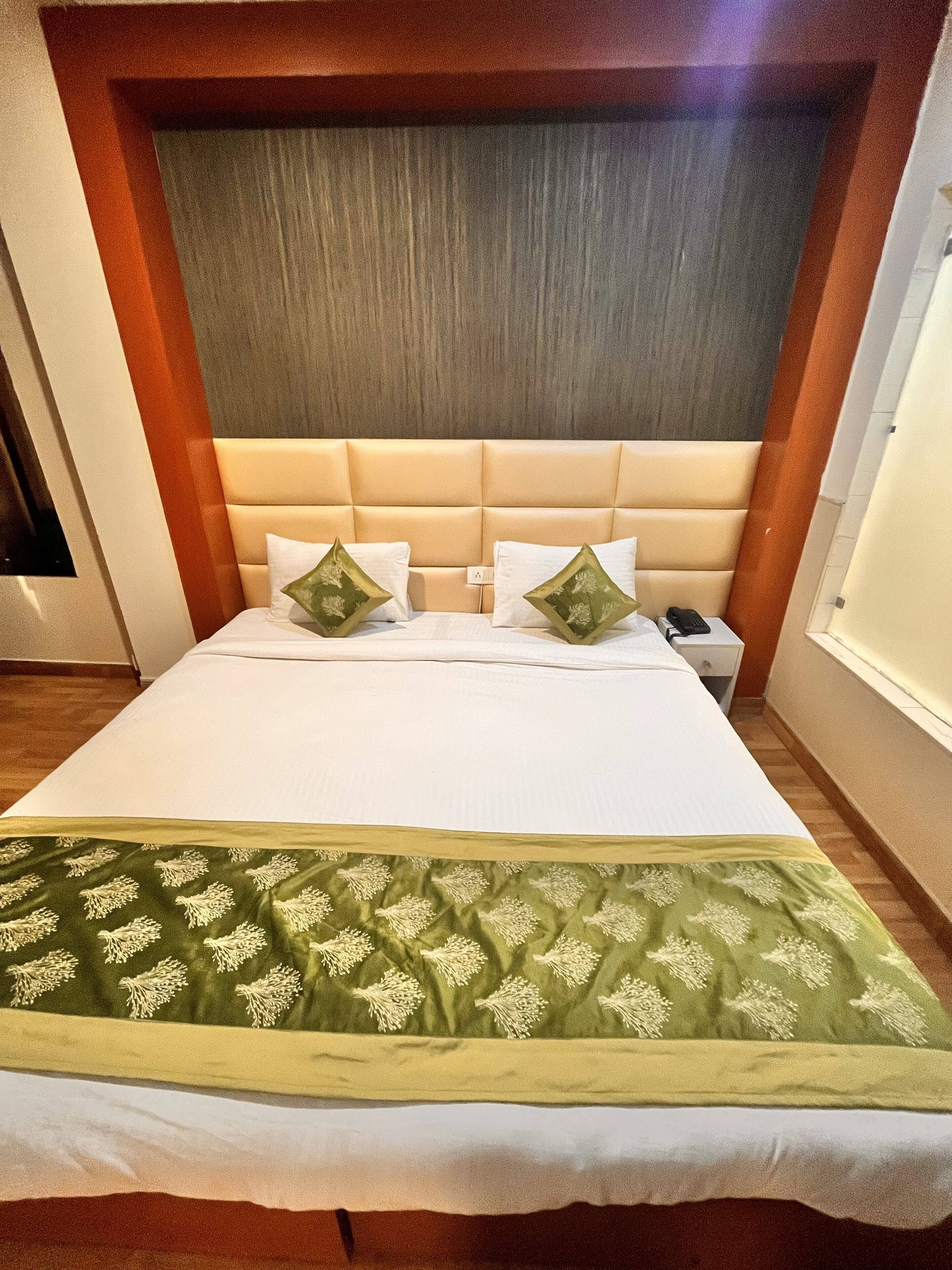 Une chambre d’hôtel avec un grand lit, une tête de lit en bois et une couvre-lit à motifs verts.