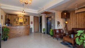 A spacious lobby with a wooden reception desk, a chandelier, leather seating, and a coffee table.