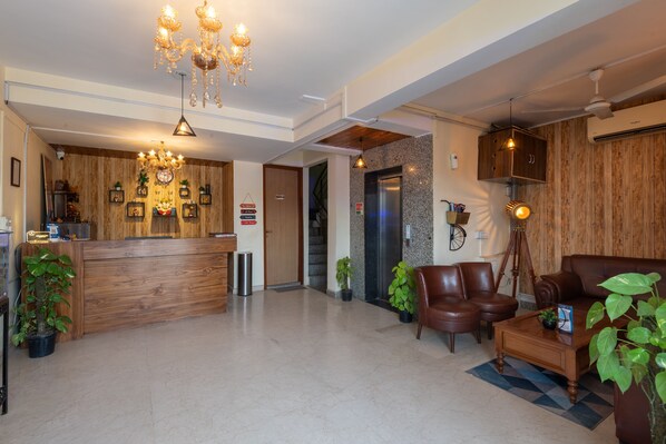A spacious lobby with a wooden reception desk, a chandelier, leather seating, and a coffee table.