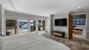 A spacious bedroom with a large bed, a TV mounted on the wall, and a view of a swimming pool through glass doors. - Stay Awhile by AvantStay | Lakefront + Pool, Dock (Mooresville)