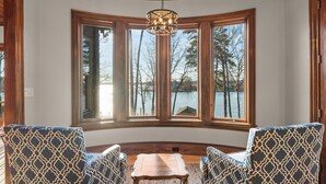 A room with a large bay window, two patterned armchairs, a wooden coffee table, and a hanging light fixture.