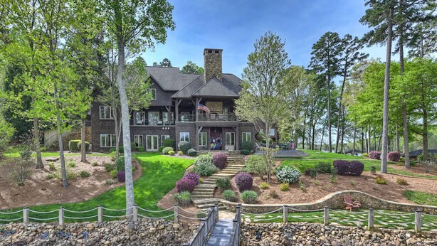 A large, two-story house with a stone chimney, surrounded by a well-maintained garden and a small pond.