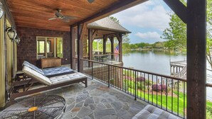 A covered outdoor area with a stone floor, a lounge chair, a small table, and a view of a lake.