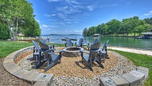 A circular seating area with Adirondack chairs around a fire pit, overlooking a lake with docks and a pier. - Private Dock, Boat Ramp, Saltwater Pool & Waterfront Firepit | Bright Water Cove (Denver)