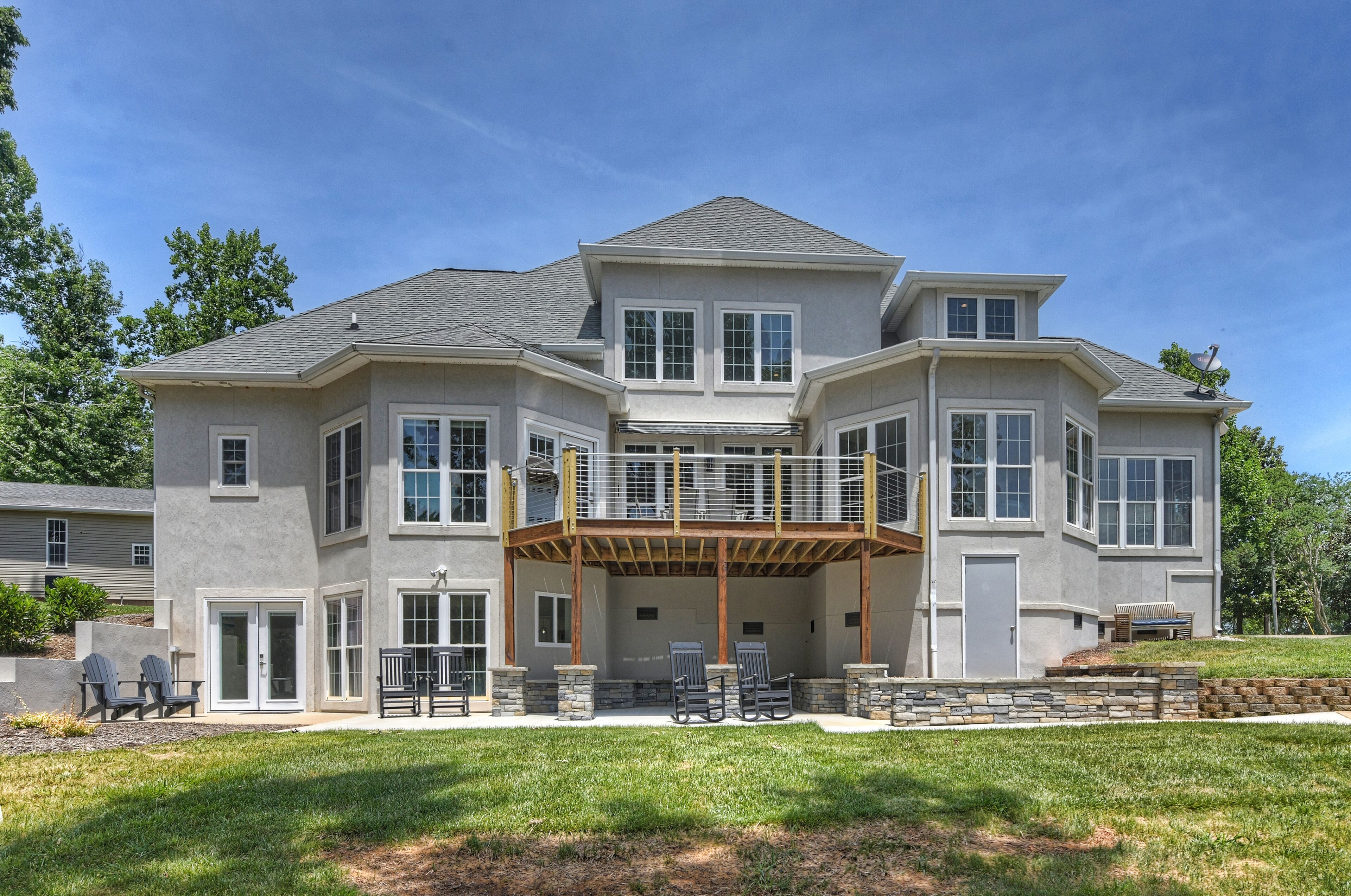 A two-story house with a covered patio, large windows, and a stone retaining wall.