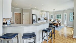 A spacious kitchen with a large island, bar stools, and a dining area with a chandelier. - Private Dock, Boat Ramp, Saltwater Pool & Waterfront Firepit | Bright Water Cove (Denver)