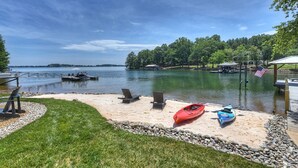 A lakeside deck with kayaks, lounge chairs, and a dock extending into the water. - Private Dock, Boat Ramp, Saltwater Pool & Waterfront Firepit | Bright Water Cove (Denver)
