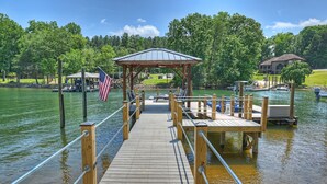 A wooden dock with a gazebo, a flag, and a boat docked in a lake surrounded by trees. - Private Dock, Boat Ramp, Saltwater Pool & Waterfront Firepit | Bright Water Cove (Denver)