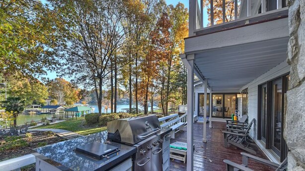 A covered outdoor deck with a grill and seating area overlooking a lake. - Lakefront Home w/ Prv. Dock, Tiki Bar & Firepit | Shore to Please by AvantStay (Denver)