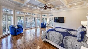 A spacious bedroom with a large bed, two blue armchairs, a ceiling fan, and a TV on the wall. - Lakefront Home w/ Prv. Dock, Tiki Bar & Firepit | Shore to Please by AvantStay (Denver)