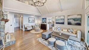 A spacious living room with a high ceiling, a chandelier, a sofa set, and artwork on the walls. - Lakefront Retreat • Hot Tub + Game Room + Dock | A Frame of Mind (Sherrills Ford)