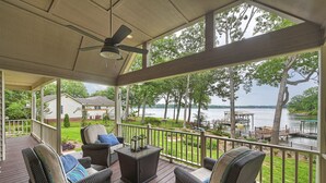 A covered outdoor deck with wicker furniture, a ceiling fan, and a view of a lake and trees. - Lakefront Retreat • Hot Tub + Game Room + Dock | A Frame of Mind (Sherrills Ford)