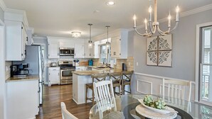 A spacious kitchen with white cabinetry, a central island, and a dining area with a glass table and chairs. - Lakefront Retreat • Hot Tub + Game Room + Dock | A Frame of Mind (Sherrills Ford)