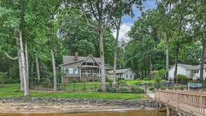 A lakeside house with a wooden deck and a dock extending into the water. - Lakefront Retreat • Hot Tub + Game Room + Dock | A Frame of Mind (Sherrills Ford)