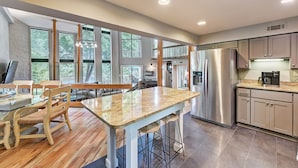 A modern kitchen with large windows, a central island, stainless steel appliances, and wooden chairs. - Lakefront w/ Private Dock + Hot Tub | Pontoon Rental | Butler Bliss by AvantStay (Sherrills Ford)