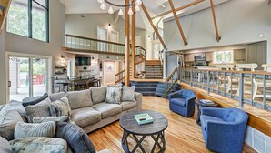 A spacious living area with a large sofa, blue armchairs, and a round coffee table. A staircase leads to an upper level with a balcony. - Lakefront w/ Private Dock + Hot Tub | Pontoon Rental | Butler Bliss by AvantStay (Sherrills Ford)