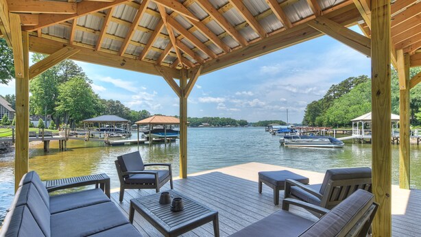 A covered deck with outdoor seating, overlooking a calm lake with boats and docks. - New Dock & Custom Home | Dock Holiday by AvantStay (Huntersville)