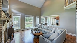 A spacious living room with a large gray sectional sofa, a wooden coffee table, and a brick fireplace. - New Dock & Custom Home | Dock Holiday by AvantStay (Huntersville)