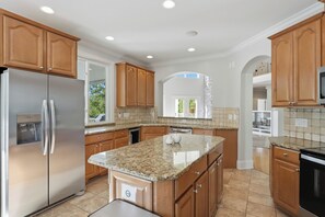 A modern kitchen with granite countertops, stainless steel appliances, wooden cabinets, and a stone backsplash.