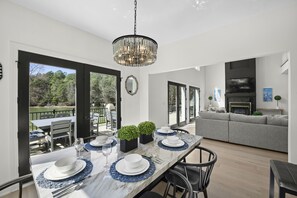 Un espace repas avec une grande table dressée pour six personnes, un lustre et une vue sur l’extérieur.