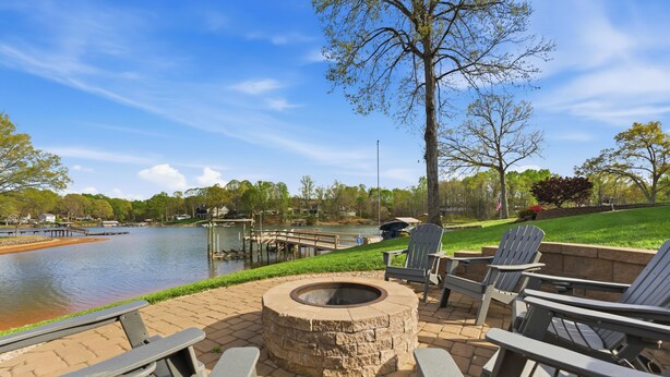A patio with Adirondack chairs, a stone fire pit, and a view of a lake with docks. - Kool Breeze by AvantStay | Boat Ramp + Hot Tub (Denver)