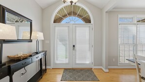 A hallway with a wooden floor, a black console table with lamps, a mirror, and a double door with a window above. - Kool Breeze by AvantStay | Boat Ramp + Hot Tub (Denver)