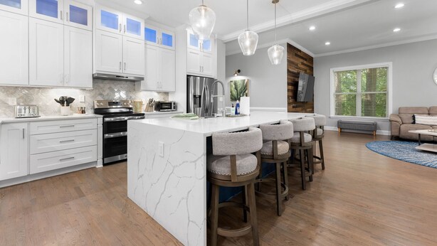 A modern kitchen with white cabinets, a marble island, and bar stools. - Laid Back Lake Life by AvantStay | Waterfront View (Mooresville)