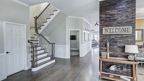 A spacious foyer with a wooden staircase, a welcome sign, and a console table with decorative items. - Laid Back Lake Life by AvantStay | Waterfront View (Mooresville)