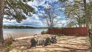A sandy beach with Adirondack chairs and a wooden fence. - Laid Back Lake Life by AvantStay | Waterfront View (Mooresville)