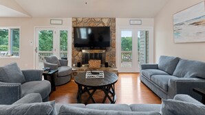 A spacious living room with a stone fireplace, grey sofas, a round coffee table, and a flat-screen TV mounted above the fireplace. - Shades of Summer by AvantStay | Gazebo, Dock, View (Denver)