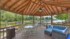 A covered deck with a table and chairs, a sofa, and a view of a lake with boats. - Shades of Summer by AvantStay | Gazebo, Dock, View (Denver)