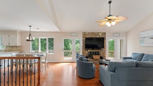 A spacious living room with a stone fireplace, a grey sofa, and a dining area with white chairs and a wooden table. - Shades of Summer by AvantStay | Gazebo, Dock, View (Denver)