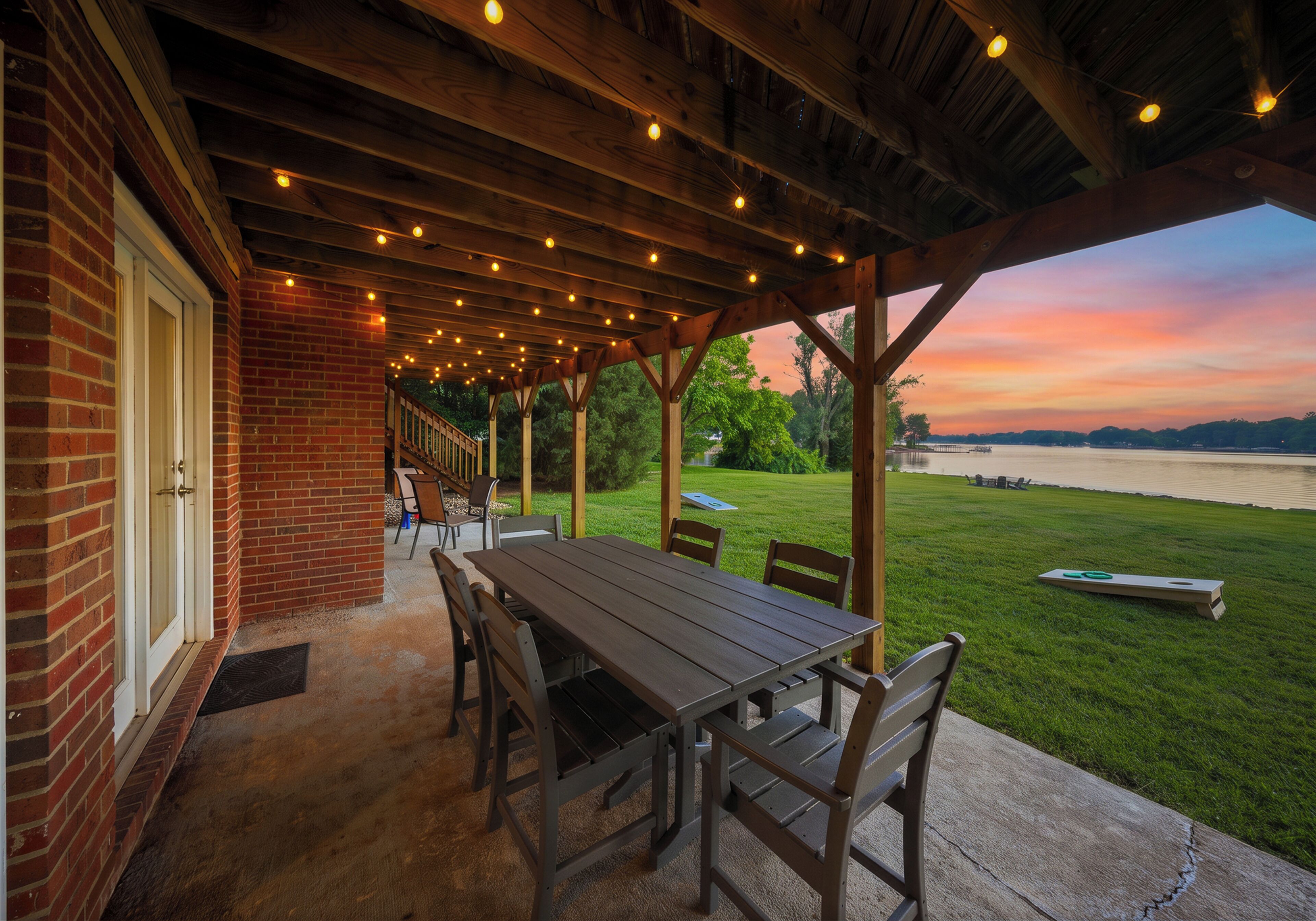 A covered patio with a table and chairs, overlooking a body of water at sunset.