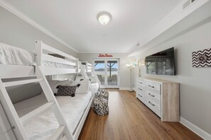 A bedroom with bunk beds, a dresser, a TV, and a door leading to a balcony.