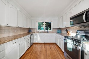 A kitchen with white cabinets, a granite countertop, a stainless steel stove, and a microwave.