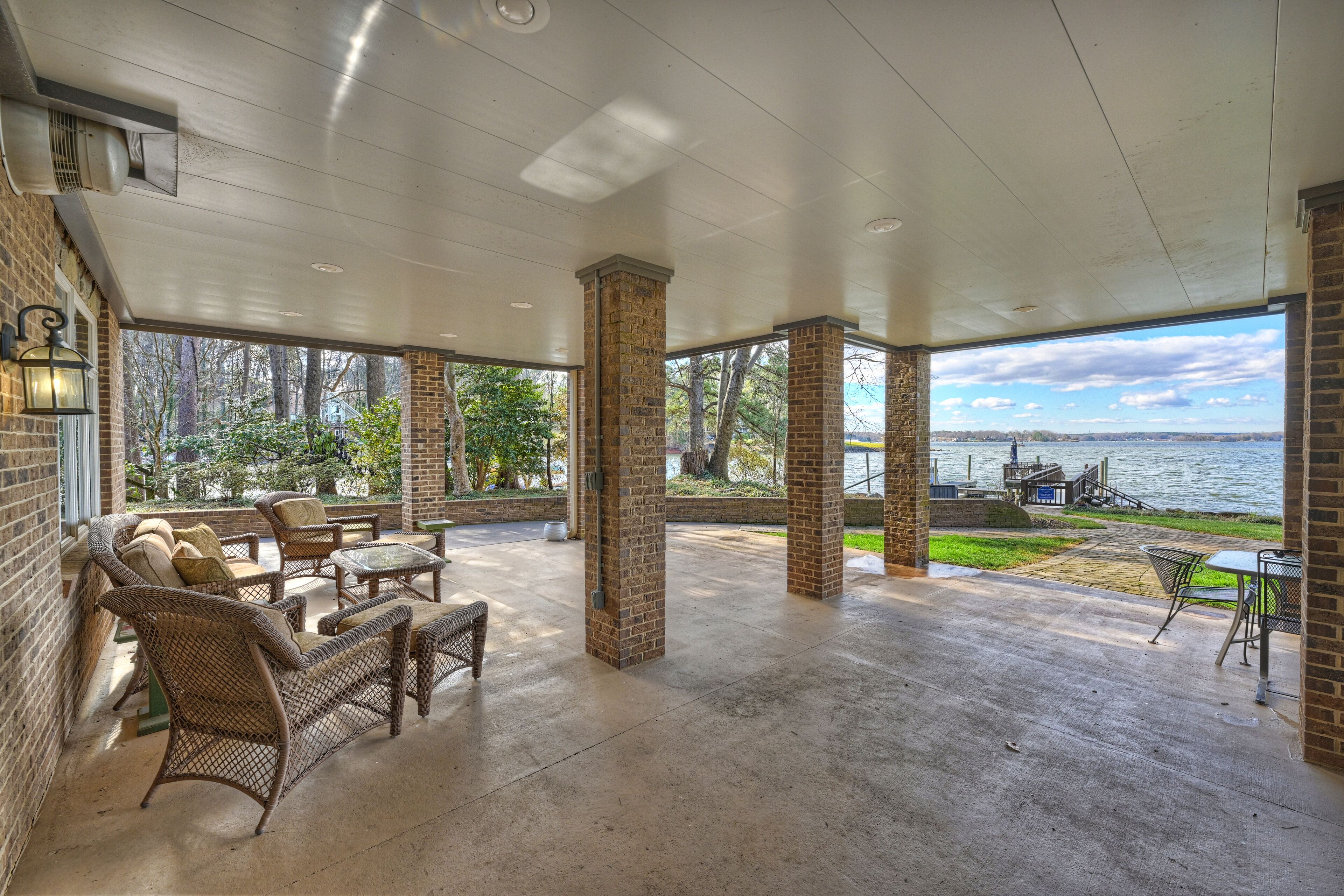 A covered patio area with wicker furniture, brick pillars, and a view of a lake.