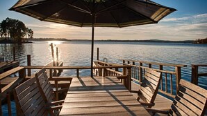 A wooden dock with benches and an umbrella, overlooking a calm lake with trees in the background. - Landover Lodge by AvantStay | Waterfront + Dock (Mooresville)