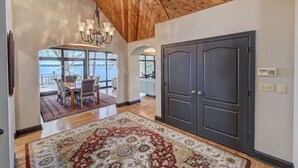 A spacious interior with a high ceiling, a large dark wooden door, and a dining area with a view. - Landover Lodge by AvantStay | Waterfront + Dock (Mooresville)