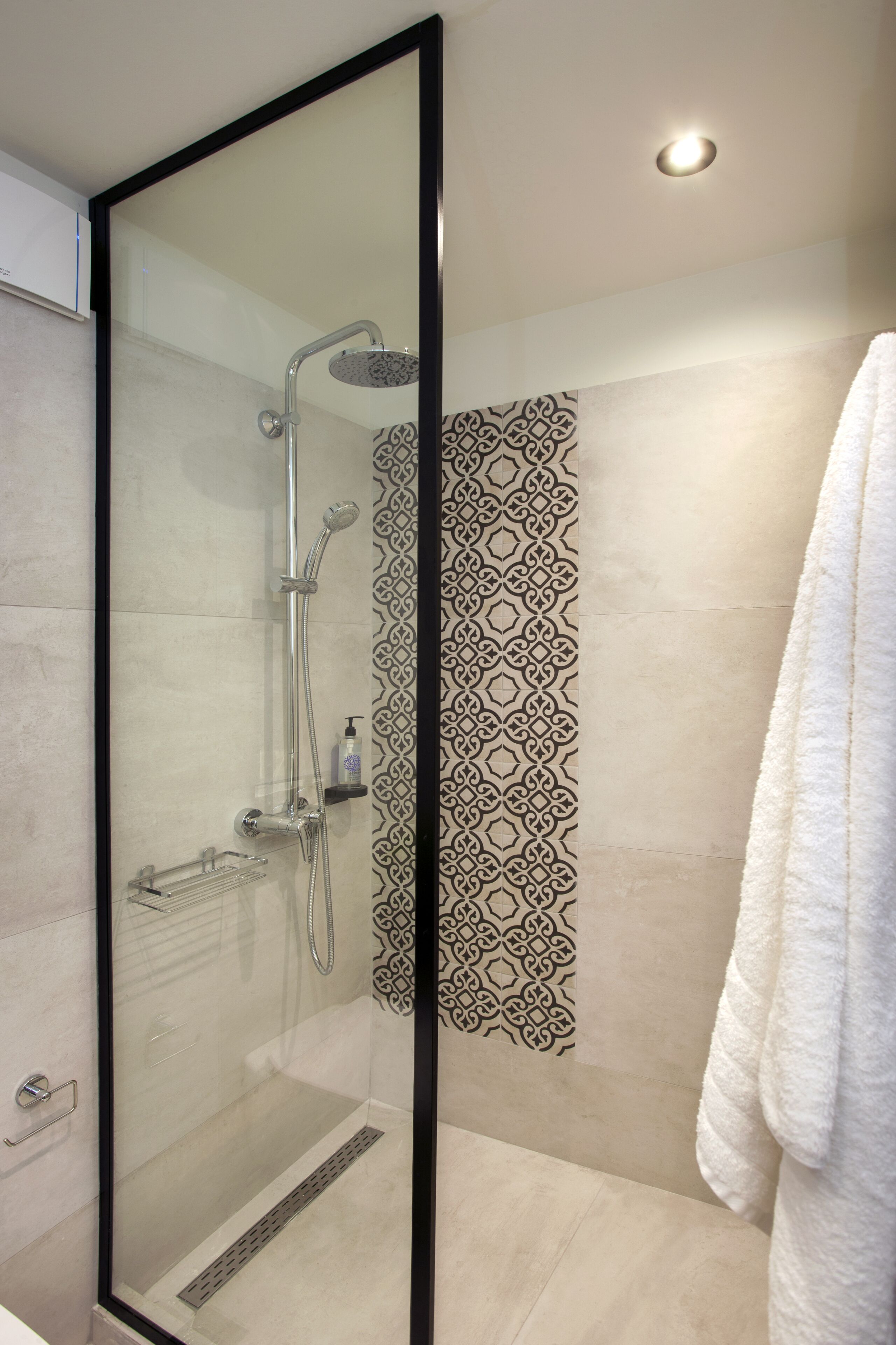 A modern bathroom with a glass-enclosed shower, a patterned wall, and a white towel hanging on the right.