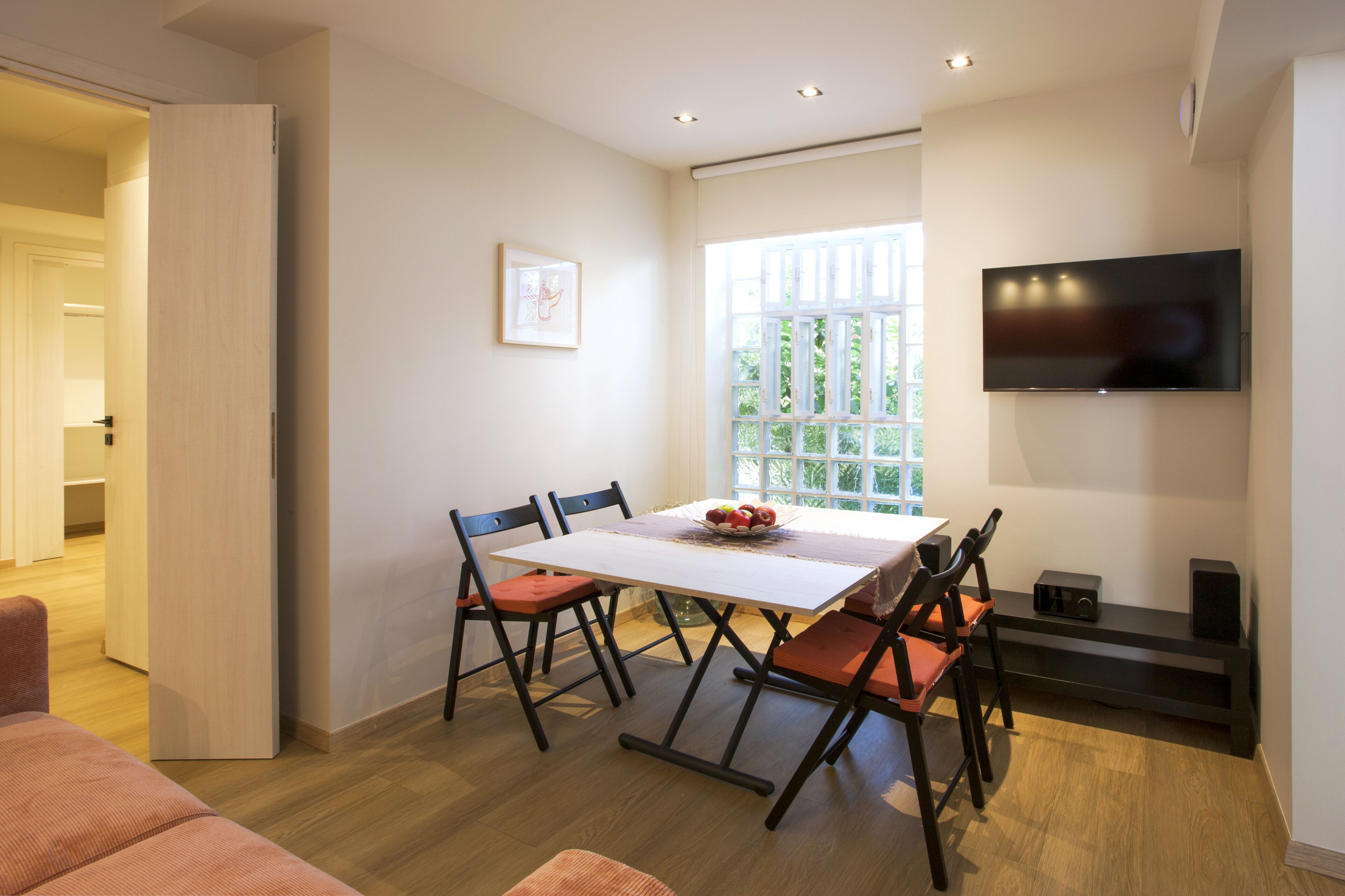 A modern dining area with a white table, black chairs, and a TV mounted on the wall.