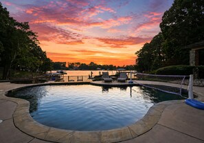 A swimming pool with lounge chairs and a view of the sunset.