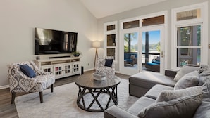 A living room with a flat-screen TV, patterned armchairs, a round coffee table, and a sectional sofa. - Lakefront Estate | Pool + Hot Tub + Dock + Sauna | Oasis at Ballycastle (Mooresville)
