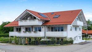 Un edificio blanco de dos pisos con techo de tejas rojas, balcones con jardineras florales y paneles solares.