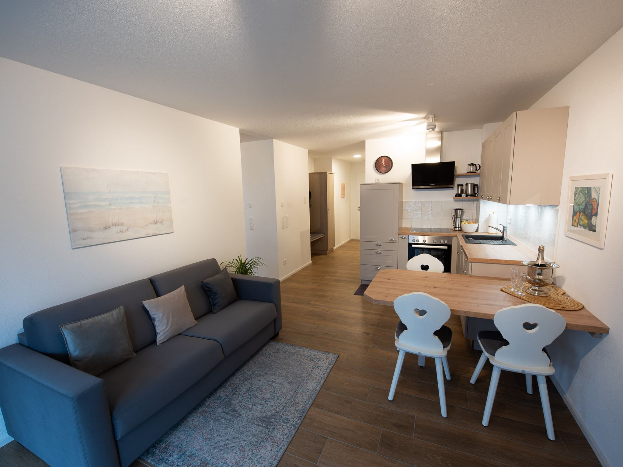 Une cuisine moderne avec un coin repas, un canapé gris et une petite table avec des chaises.