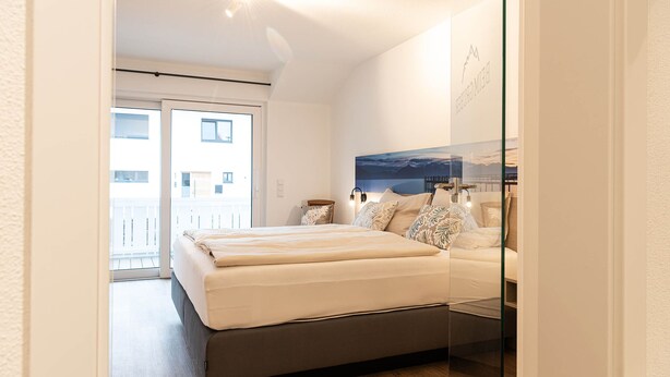 Un dormitorio moderno con una cama grande, un cristalero que da a un balcón y vistas a la ciudad.